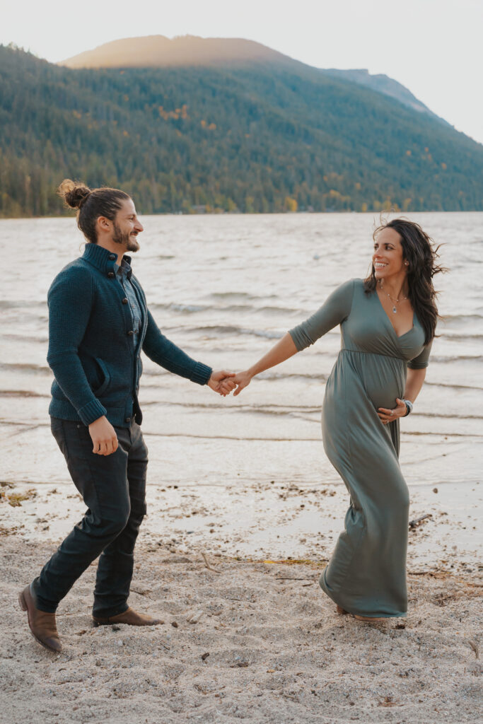 Couple holding hands, looking at each other walking on the river front with mom's hand on her bump